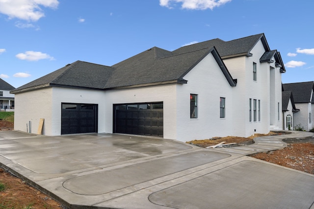 view of property exterior featuring driveway, brick siding, roof with shingles, and an attached garage