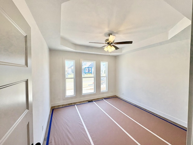 spare room featuring ceiling fan, a tray ceiling, and baseboards