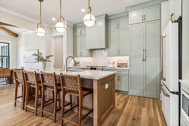 kitchen with sink, hanging light fixtures, white refrigerator, a center island with sink, and light wood-type flooring