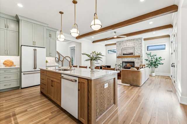 kitchen featuring sink, backsplash, white appliances, a fireplace, and a center island with sink