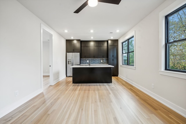 kitchen featuring stainless steel fridge, light hardwood / wood-style floors, plenty of natural light, and an island with sink