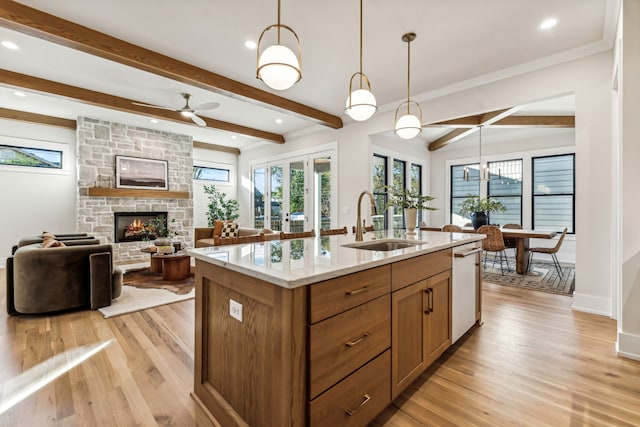 kitchen featuring sink, beam ceiling, decorative light fixtures, light hardwood / wood-style flooring, and an island with sink