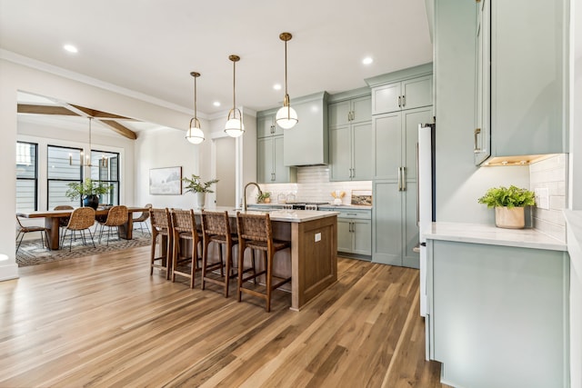 kitchen with a breakfast bar, a center island with sink, beamed ceiling, decorative light fixtures, and wood-type flooring