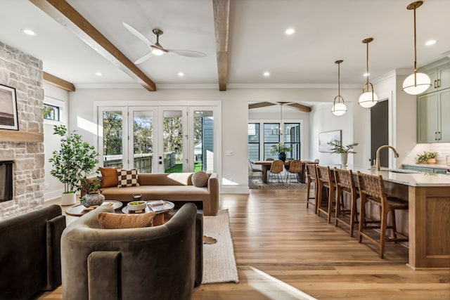 living room featuring ceiling fan, sink, beam ceiling, a fireplace, and light hardwood / wood-style floors