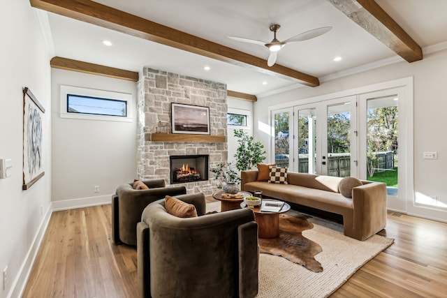 living room featuring a stone fireplace, ceiling fan, light wood-type flooring, ornamental molding, and beam ceiling