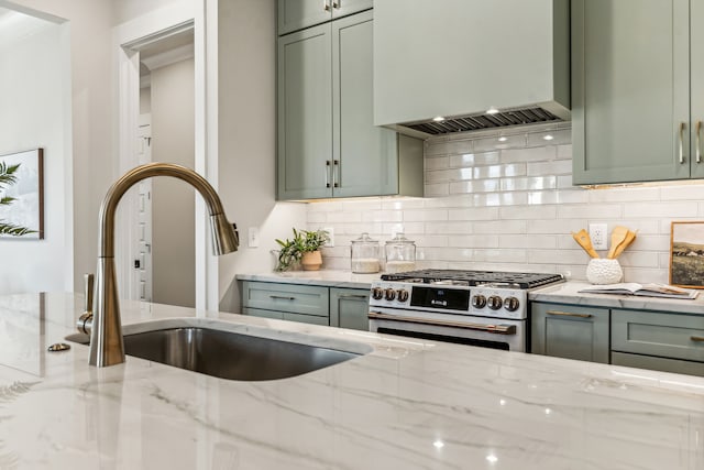 kitchen featuring high end stove, green cabinets, light stone countertops, and custom range hood