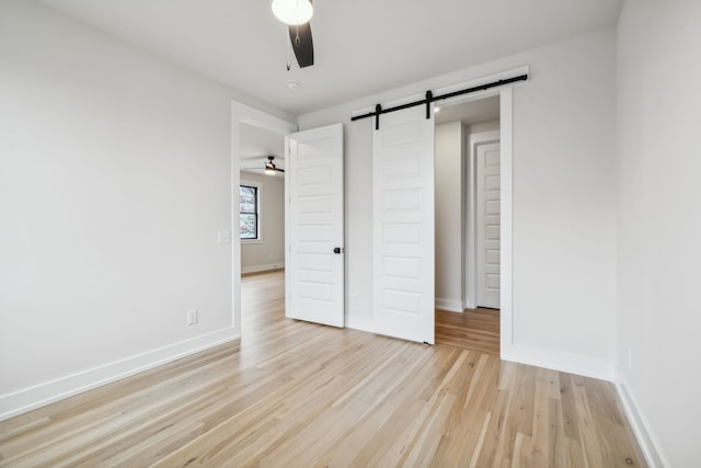 unfurnished bedroom featuring light wood-type flooring, a barn door, a closet, and ceiling fan