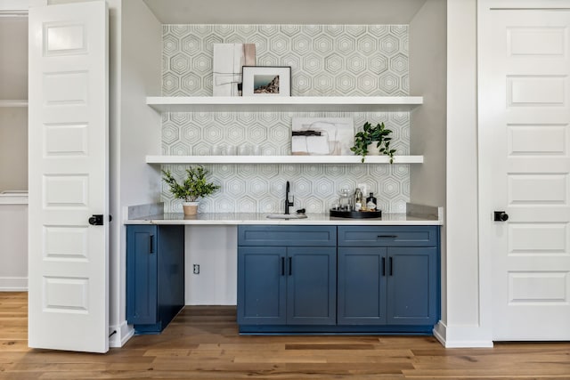 bar featuring backsplash, sink, wood-type flooring, and blue cabinetry