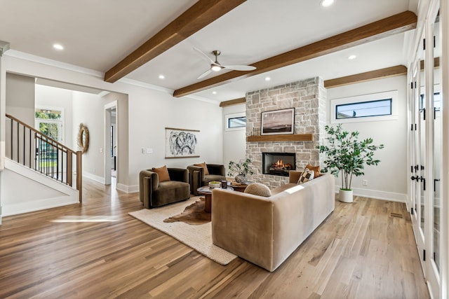 living room with french doors, ceiling fan, beamed ceiling, light hardwood / wood-style floors, and a stone fireplace