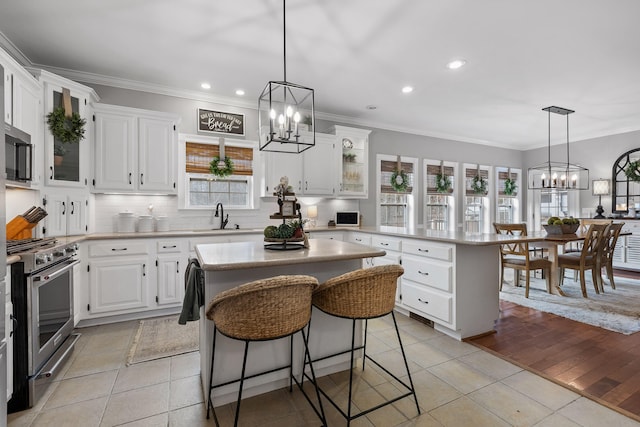 kitchen with appliances with stainless steel finishes, a kitchen island, white cabinetry, light tile patterned floors, and a breakfast bar area