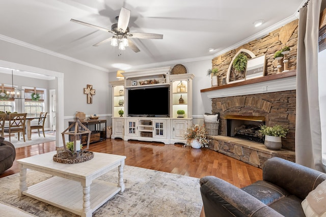 living room featuring ceiling fan, hardwood / wood-style floors, ornamental molding, and a stone fireplace