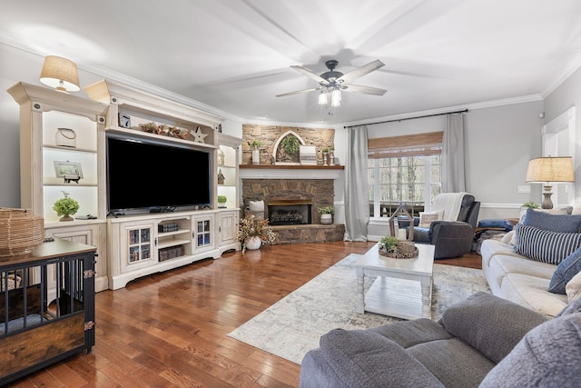 living room with ceiling fan, a stone fireplace, crown molding, and dark hardwood / wood-style flooring