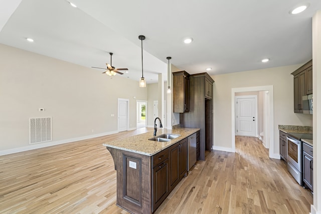 kitchen with appliances with stainless steel finishes, light wood-type flooring, light stone counters, dark brown cabinets, and sink