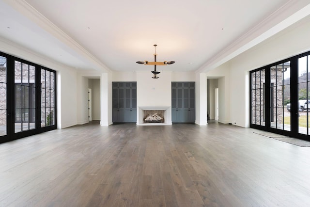 unfurnished living room featuring a wealth of natural light, a chandelier, wood finished floors, and ornamental molding