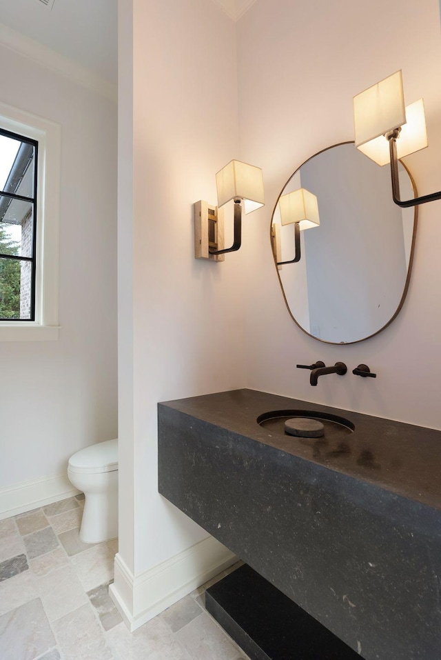 bathroom featuring toilet, ornamental molding, a sink, stone finish flooring, and baseboards