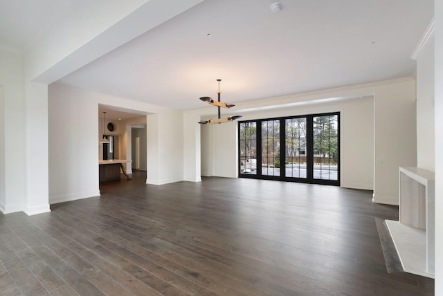 unfurnished living room featuring dark wood finished floors, an inviting chandelier, baseboards, and ornamental molding