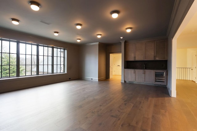 unfurnished living room with beverage cooler, baseboards, visible vents, ornamental molding, and dark wood-type flooring