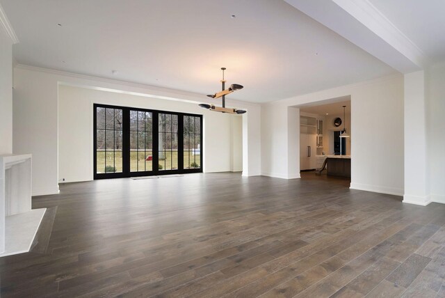 unfurnished living room with baseboards, a notable chandelier, dark wood finished floors, and crown molding