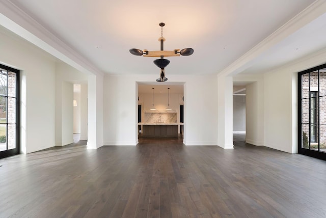 unfurnished living room featuring an inviting chandelier, crown molding, dark wood-style flooring, and baseboards