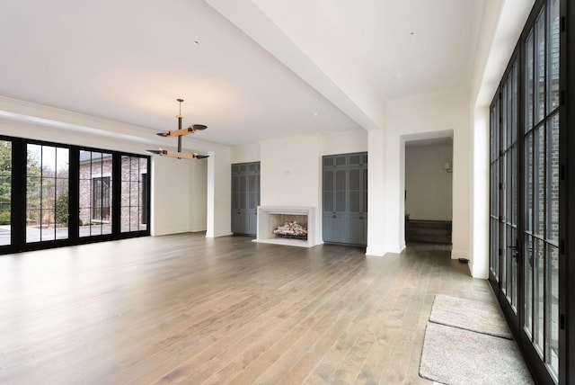 unfurnished living room with an inviting chandelier, a fireplace, light wood-type flooring, and baseboards