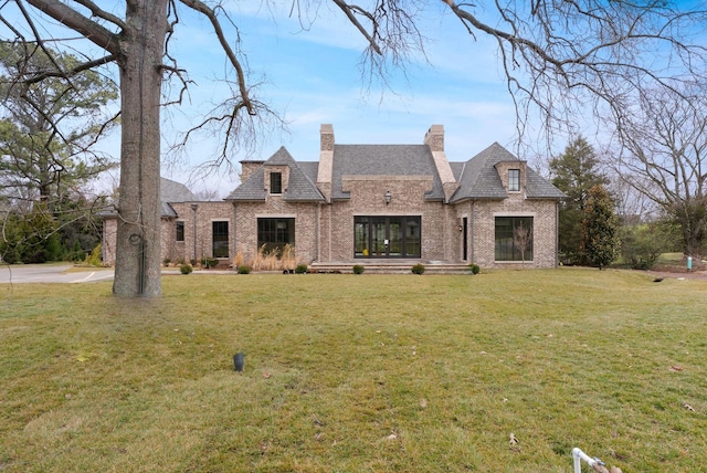 french country inspired facade with brick siding, a chimney, and a front yard