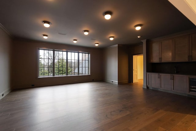 unfurnished living room with dark wood finished floors, crown molding, and baseboards