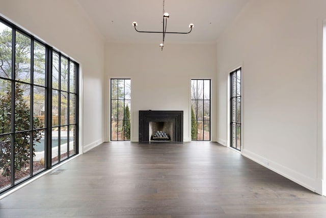 unfurnished living room featuring wood finished floors, visible vents, baseboards, an inviting chandelier, and a fireplace