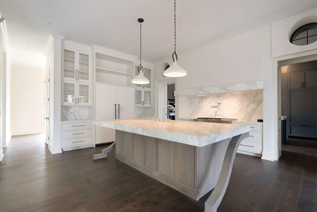 kitchen with tasteful backsplash, glass insert cabinets, dark wood finished floors, light countertops, and a large island with sink