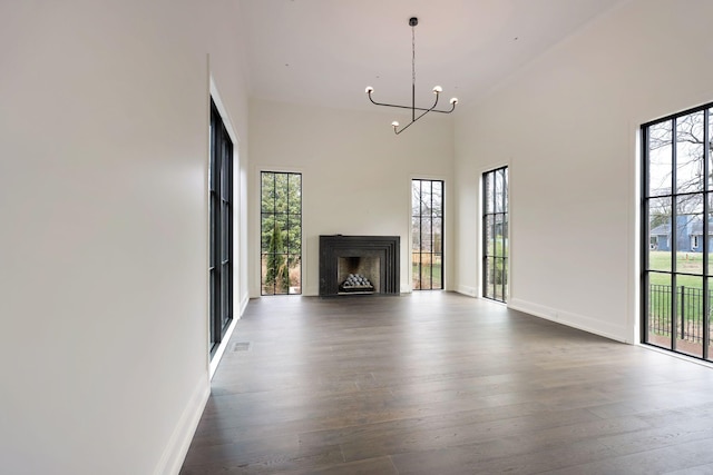 unfurnished living room with an inviting chandelier, a towering ceiling, wood finished floors, and a wealth of natural light