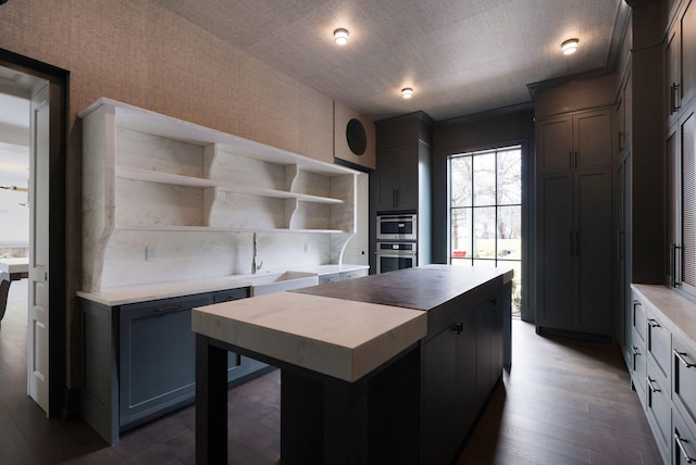 kitchen with open shelves, a sink, dark wood finished floors, a center island, and light countertops