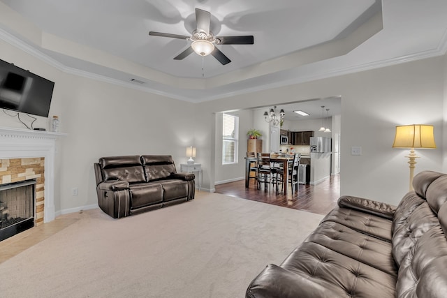 living room featuring a raised ceiling, a stone fireplace, ornamental molding, and wood-type flooring