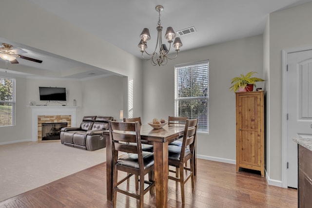 dining space featuring a fireplace, light wood-type flooring, ceiling fan with notable chandelier, and crown molding