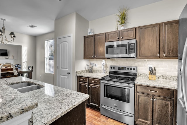 kitchen with dark brown cabinets, stainless steel appliances, light stone counters, and sink