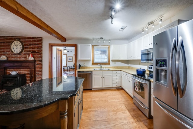 kitchen with appliances with stainless steel finishes, a textured ceiling, beamed ceiling, white cabinets, and light hardwood / wood-style floors