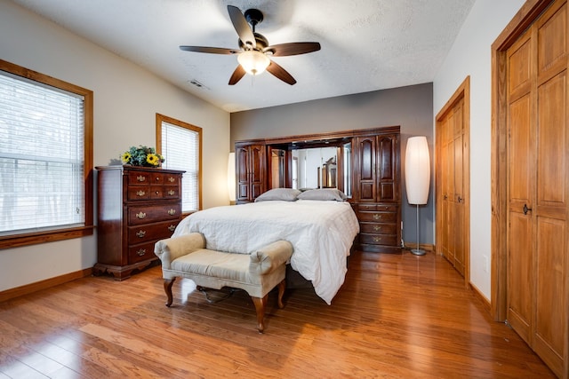 bedroom with ceiling fan, light hardwood / wood-style floors, a textured ceiling, and multiple closets