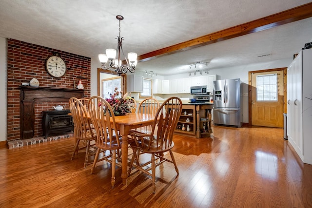 dining area with beamed ceiling, a chandelier, a textured ceiling, and light hardwood / wood-style flooring