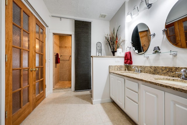 bathroom featuring tile patterned floors, vanity, a textured ceiling, and tiled shower