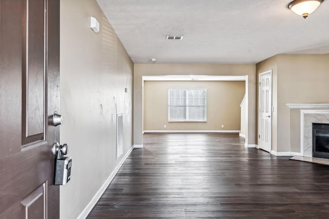 unfurnished living room with a high end fireplace, a textured ceiling, and dark wood-type flooring