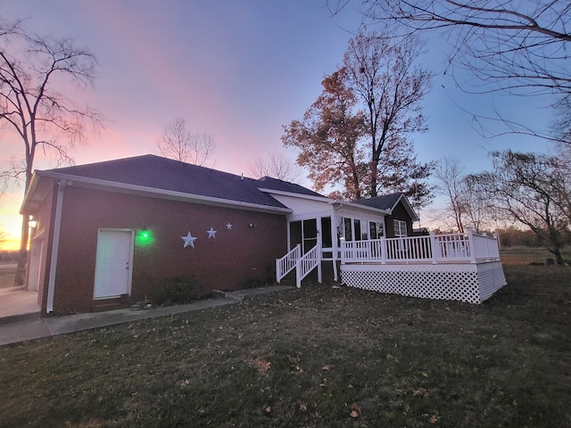 back house at dusk with a yard, a deck, and a sunroom