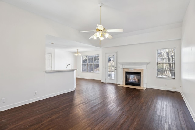 unfurnished living room with sink, dark hardwood / wood-style floors, ceiling fan with notable chandelier, and a premium fireplace