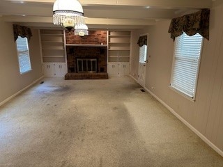 unfurnished living room with carpet, a brick fireplace, and a notable chandelier