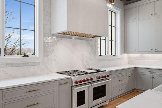 kitchen with premium range hood, range with two ovens, plenty of natural light, and light stone countertops