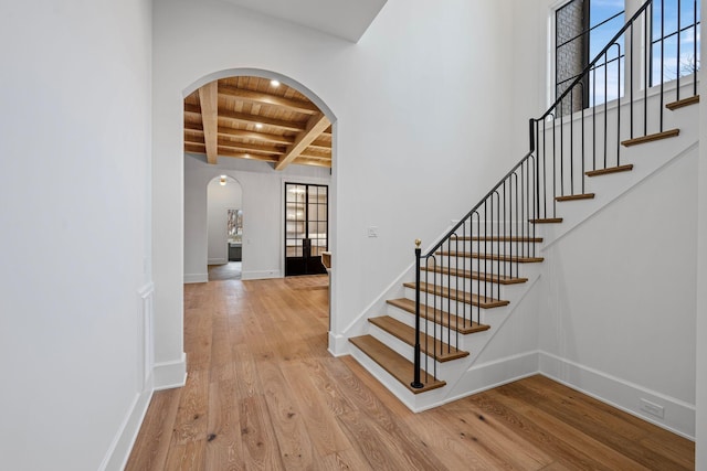 staircase with baseboards, arched walkways, wooden ceiling, wood finished floors, and beam ceiling