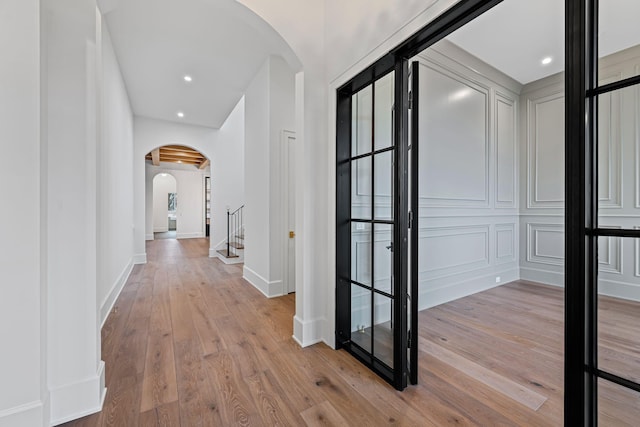 hallway featuring light wood-type flooring, arched walkways, baseboards, and recessed lighting