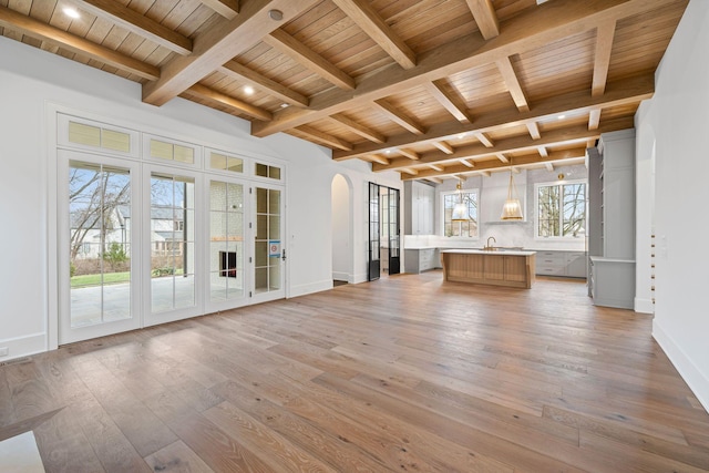 unfurnished living room featuring arched walkways, wood ceiling, light wood-style flooring, and beam ceiling