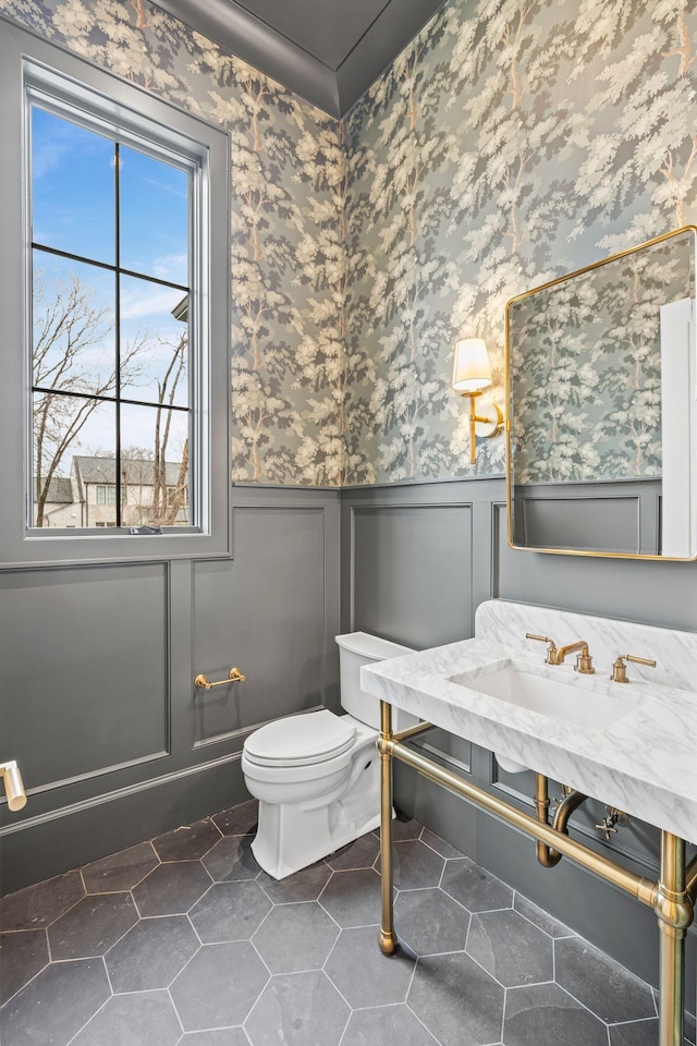 bathroom featuring toilet, wallpapered walls, tile patterned flooring, and wainscoting