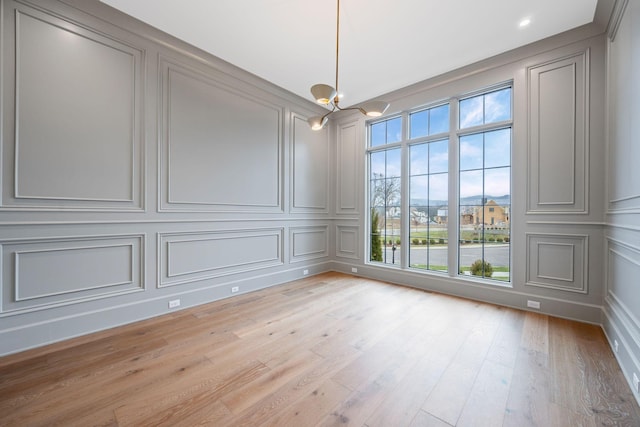 unfurnished dining area featuring a chandelier, a decorative wall, and light wood-style flooring