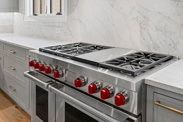 kitchen with light wood-style flooring, high end stainless steel range, gray cabinets, decorative backsplash, and light stone countertops