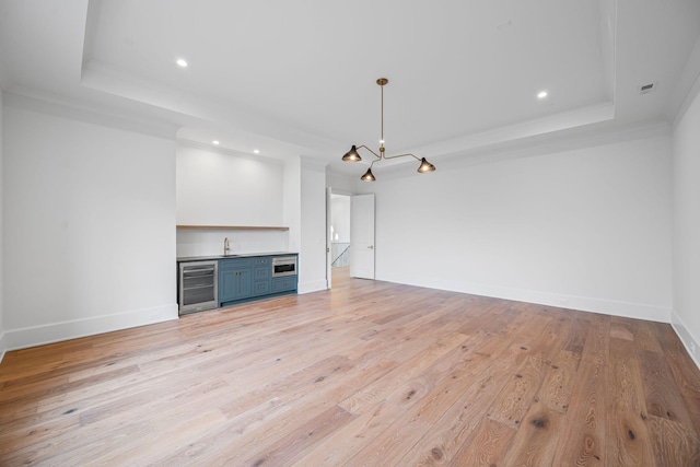 unfurnished living room with wine cooler, baseboards, light wood-type flooring, wet bar, and a tray ceiling