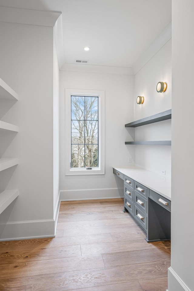 interior space with built in desk, light wood-style flooring, baseboards, and crown molding